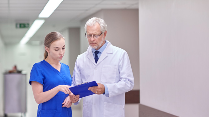 Older male doctor reviewing clipboard with medical student